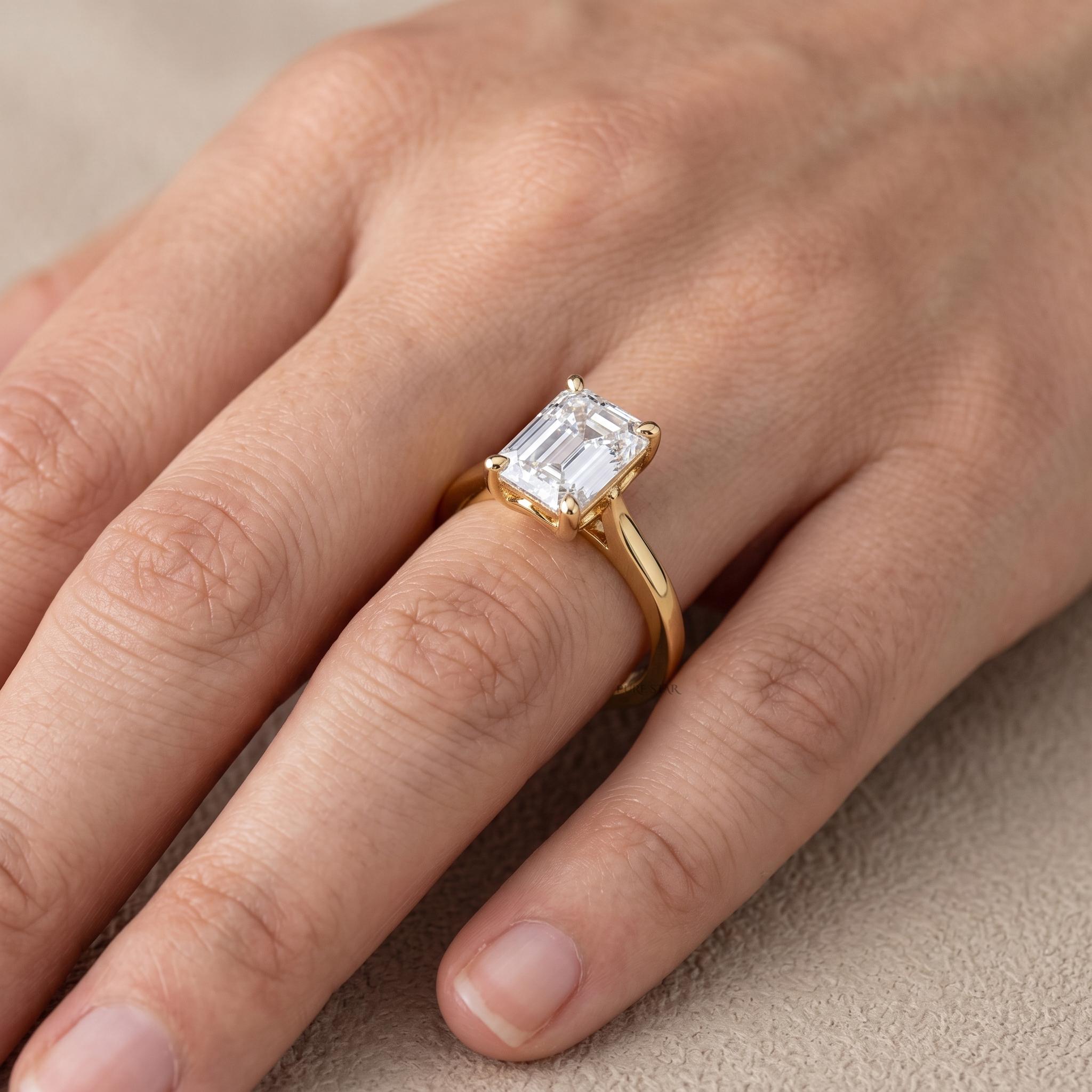 Emerald cut lab diamond solitaire ring with polished yellow gold band viewed from the side.